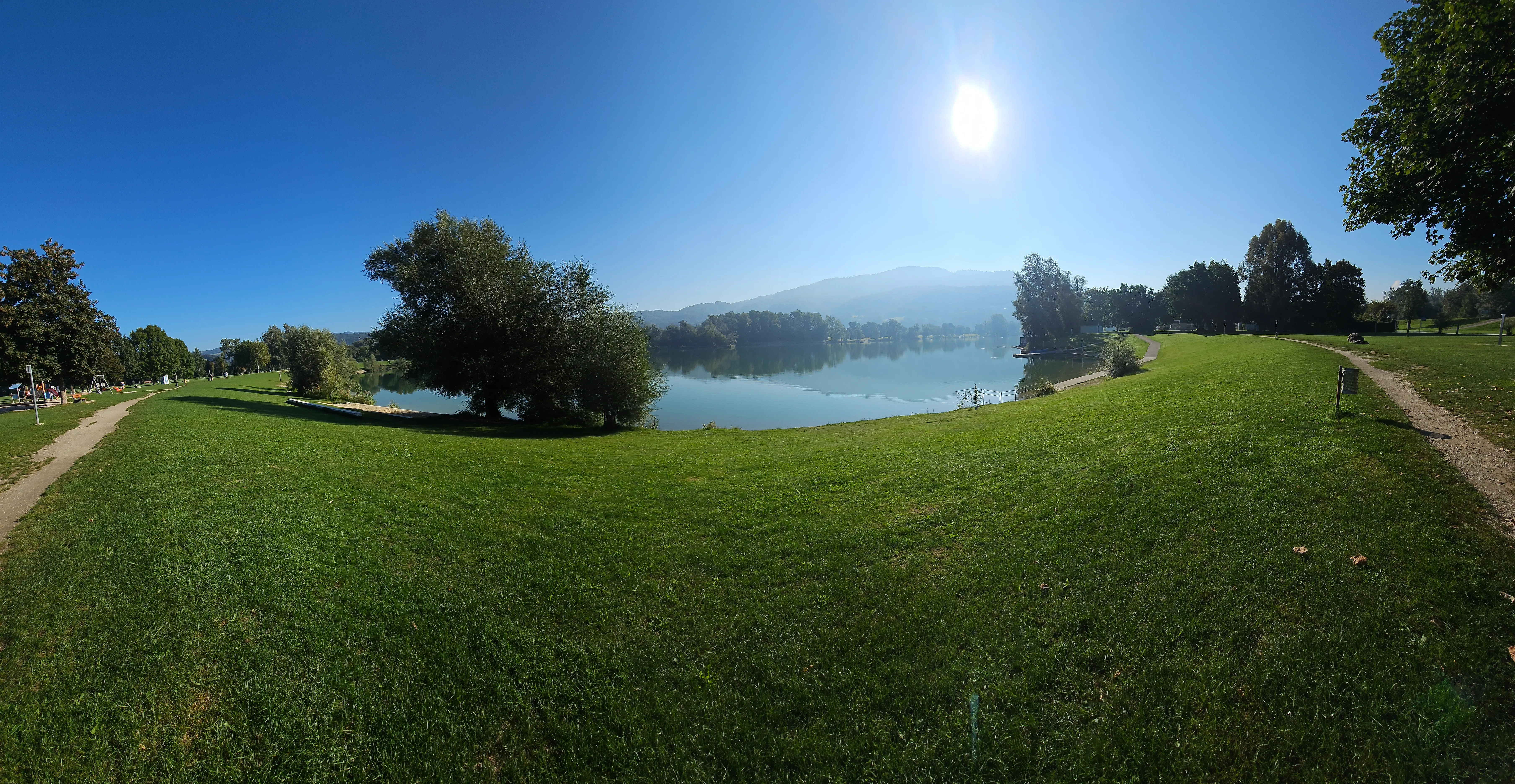 Pleschinger See mit Wiese und Hügeln im Morgendunst